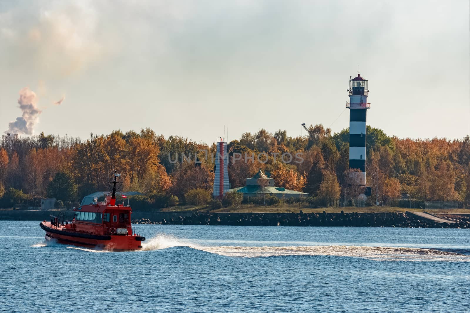 Red pilot ship moving at speed past the lighthouse in Riga