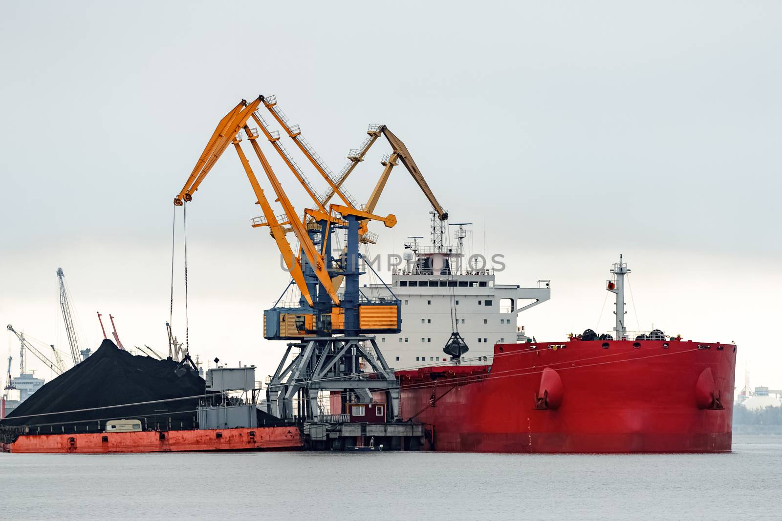 Large red cargo ship loading with a coal in the port