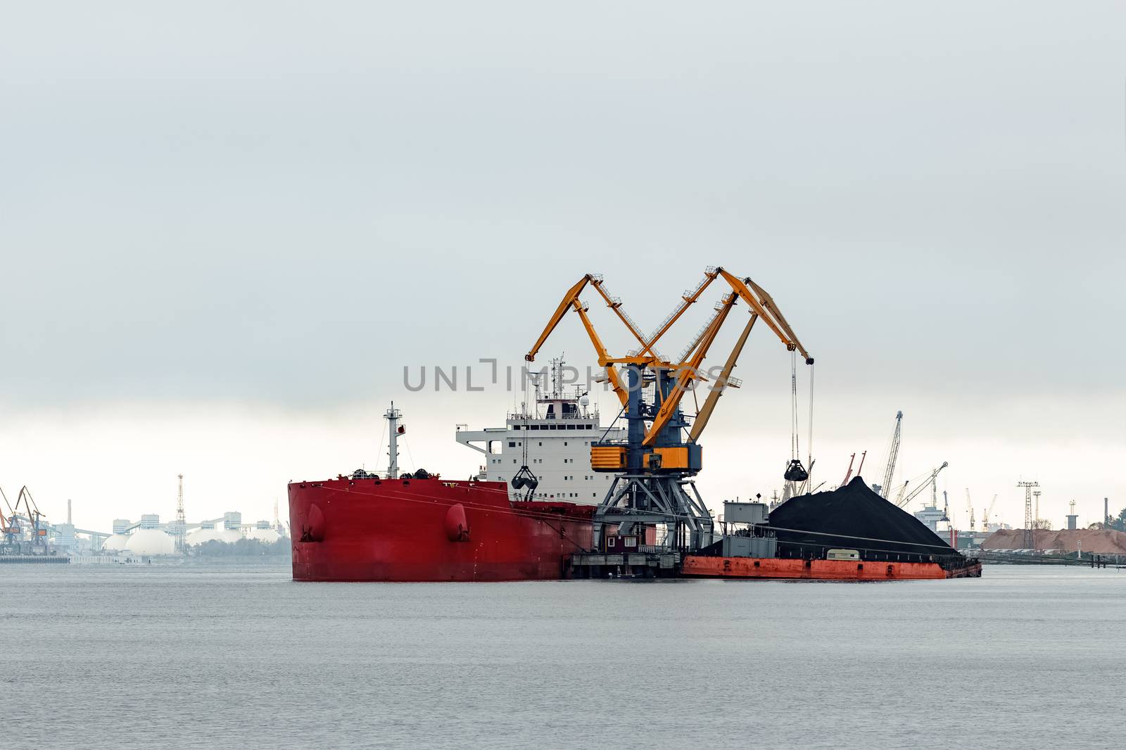 Large red cargo ship loading with a coal in the port