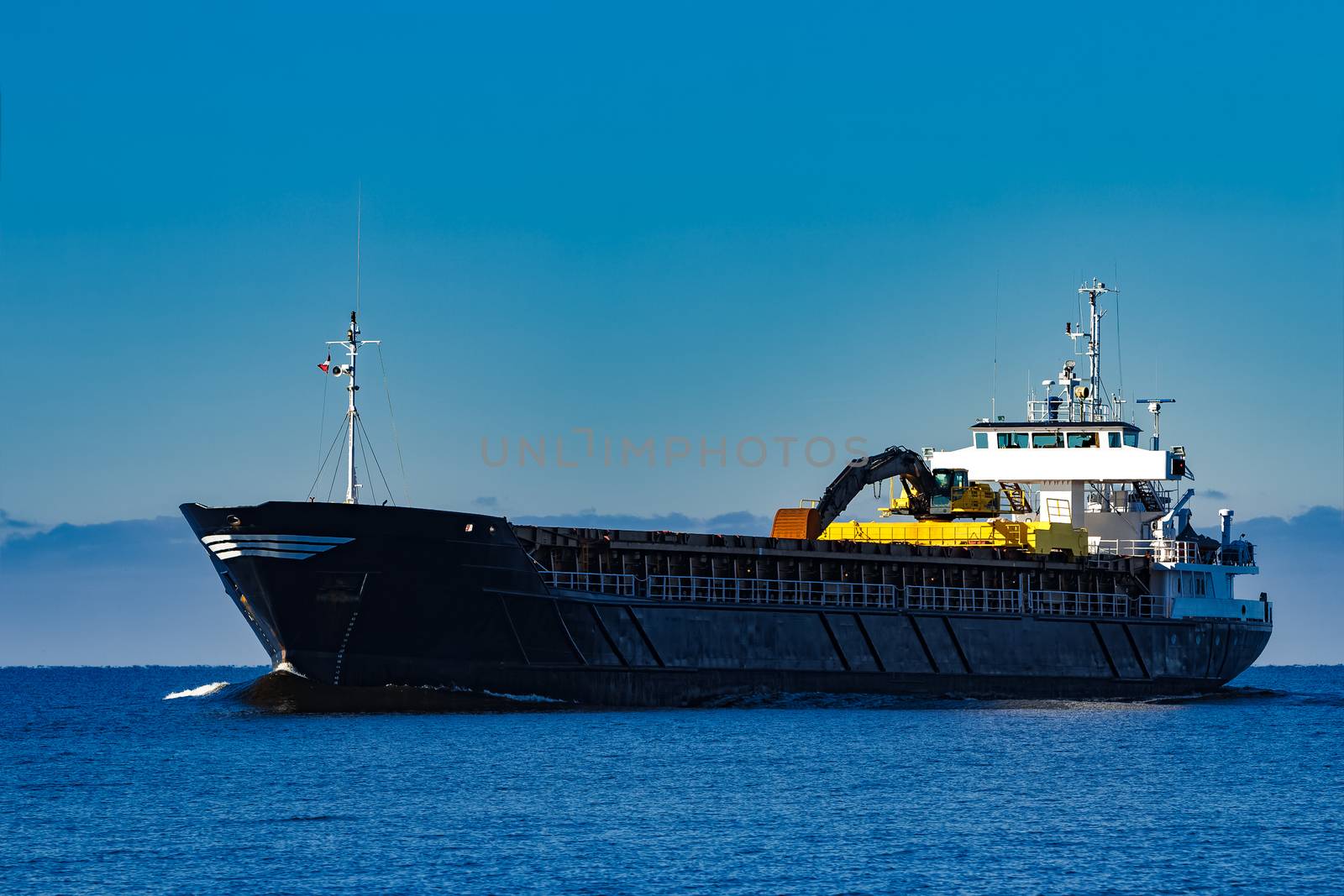 Black cargo ship with long reach excavator moving by baltic sea