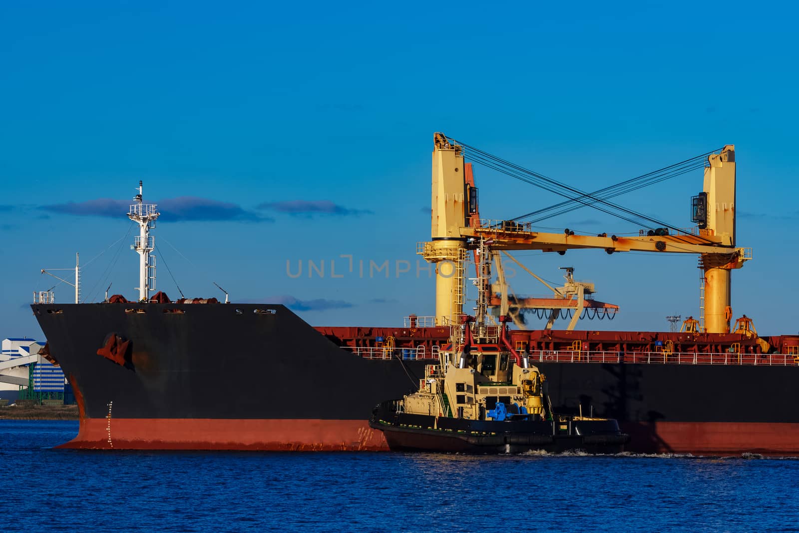 Black cargo ship mooring at the port with tug ship support