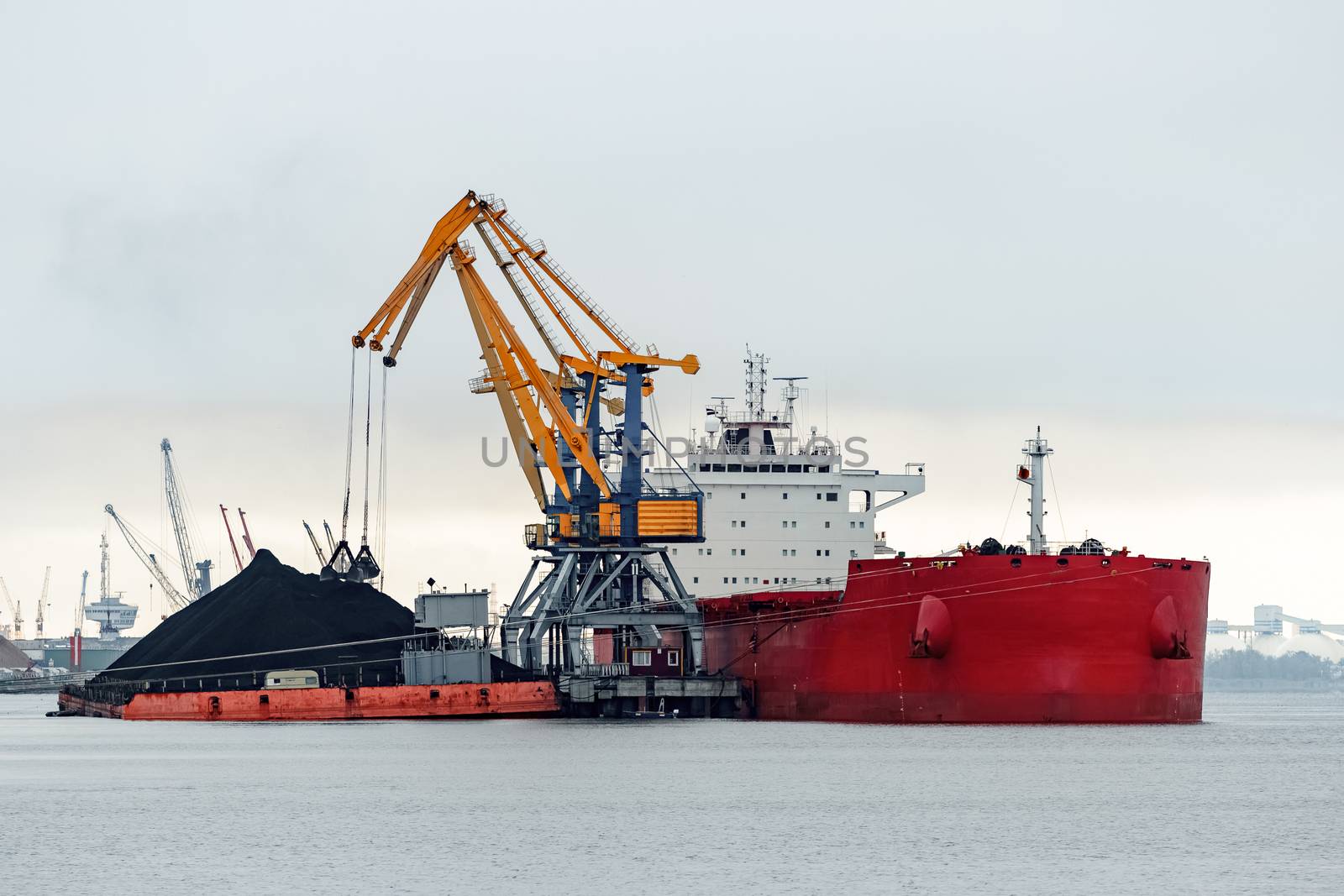 Large red cargo ship loading with a coal in the port