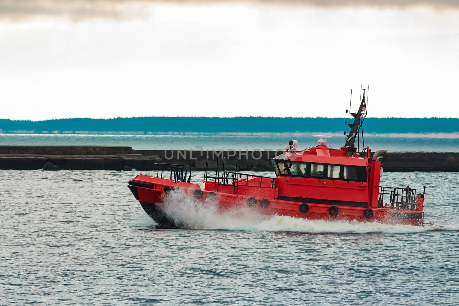 Red pilot ship sailing to Baltic sea past the breakwater dam