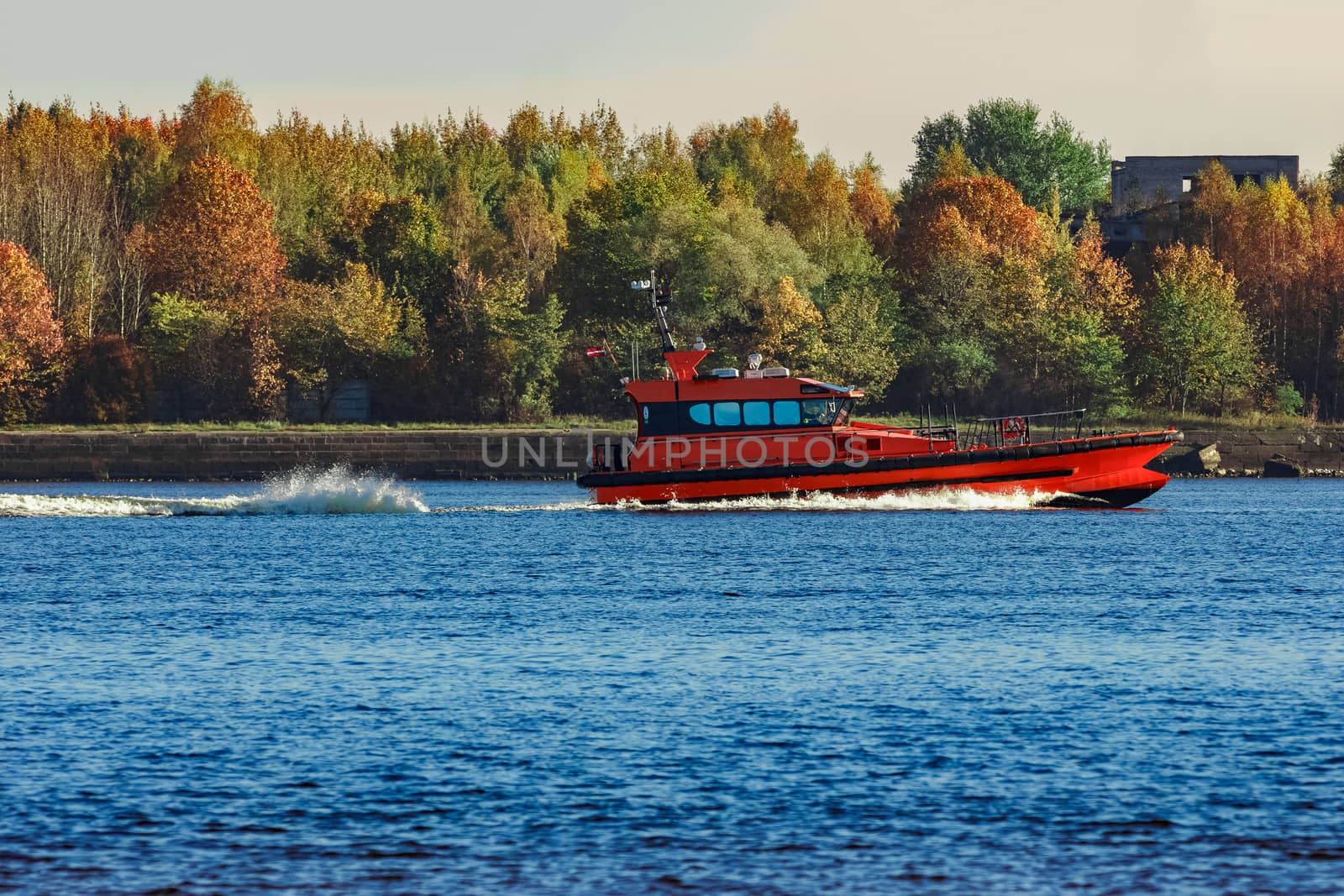 Red pilot ship moving past the autumn trees in Europe