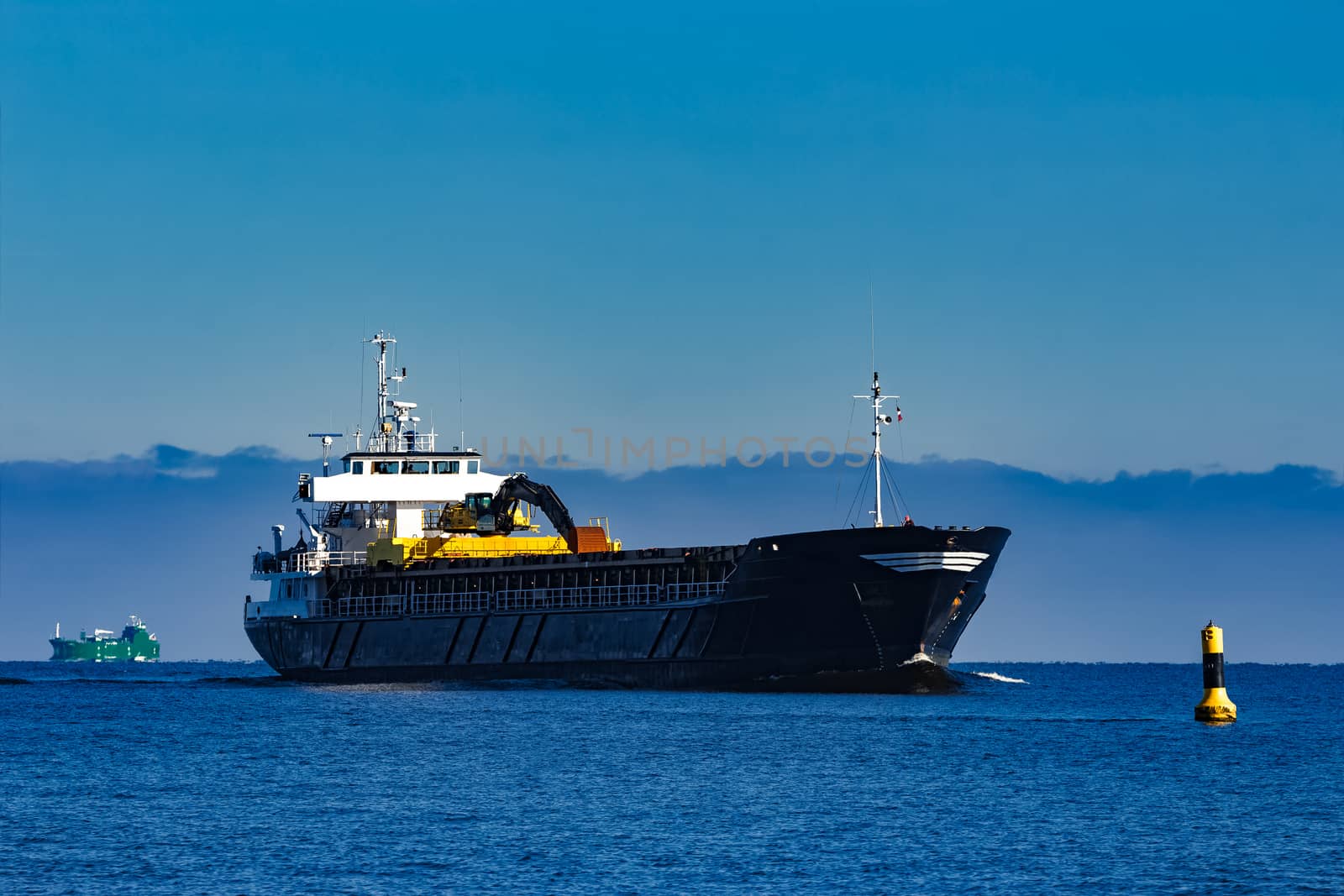 Black cargo ship with long reach excavator moving by baltic sea