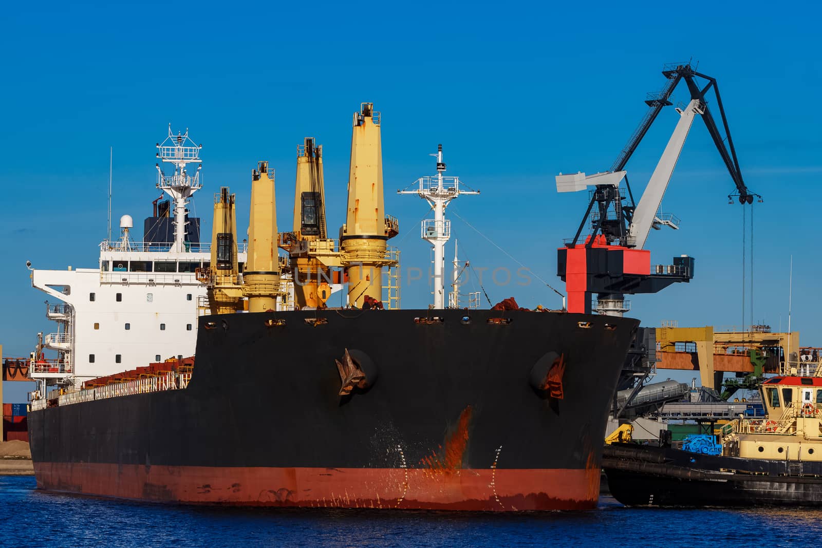 Black cargo ship mooring at the port with tug ship support