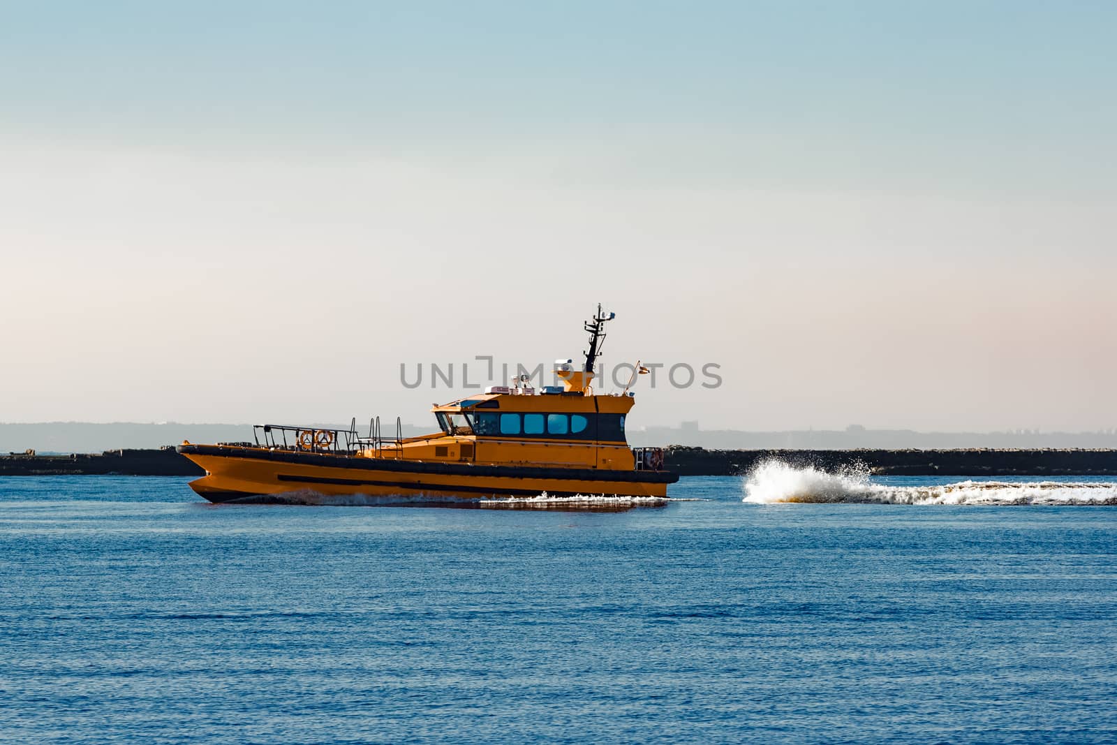 Orange pilot ship moving at speed past the breakwater dam