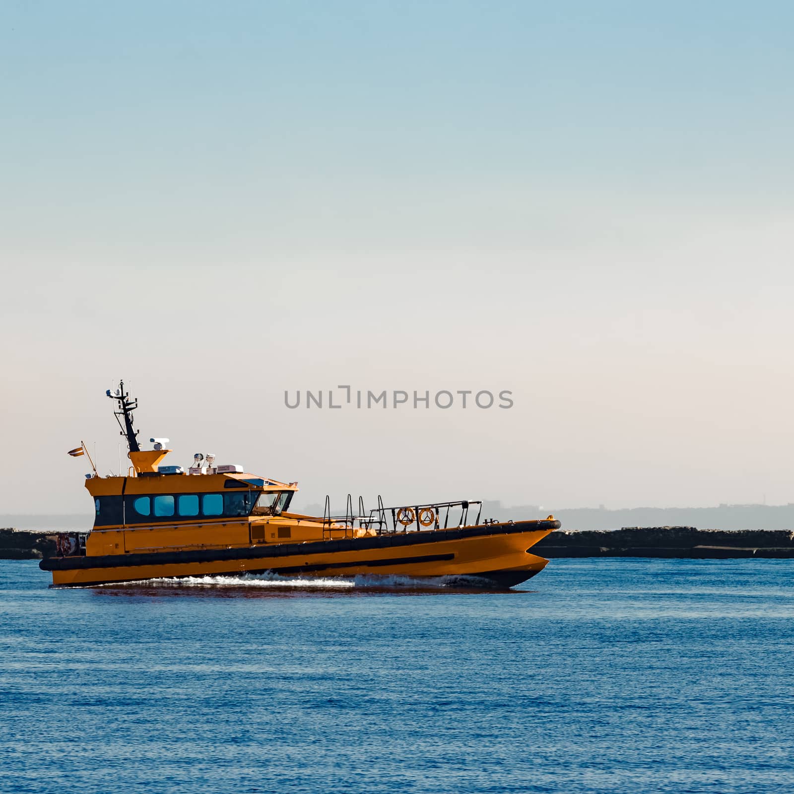 Orange pilot ship moving at speed past the breakwater dam