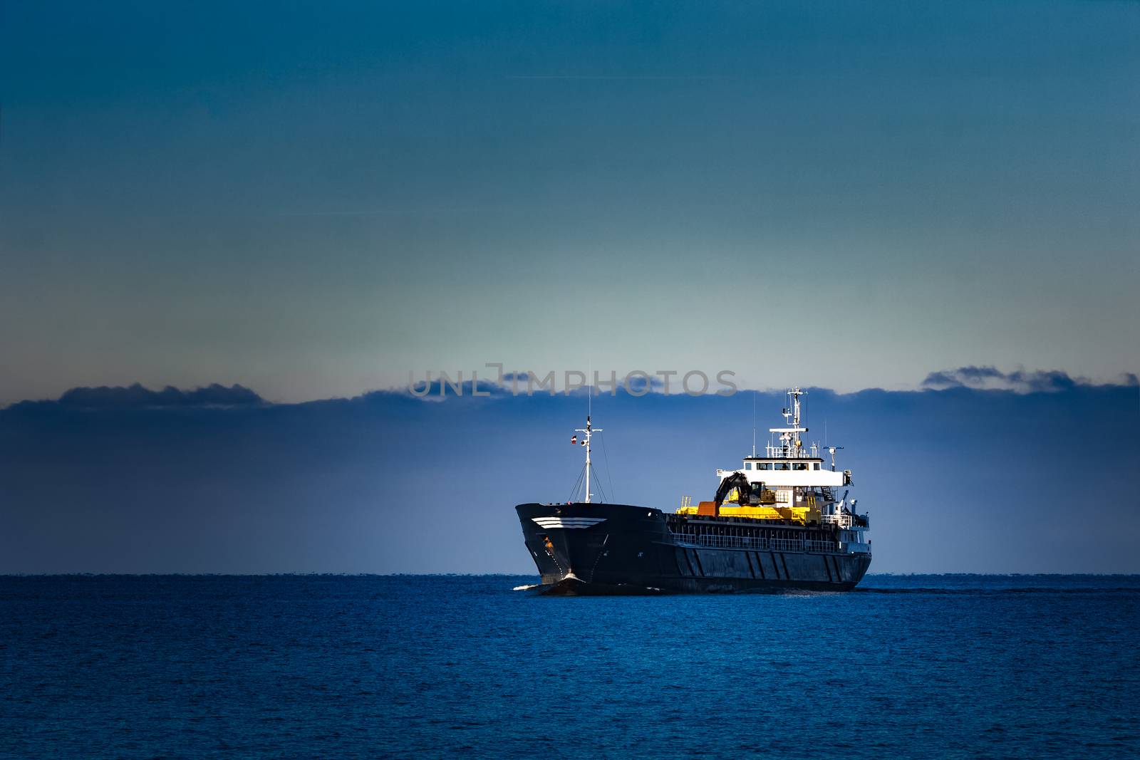 Black cargo ship with long reach excavator moving by baltic sea