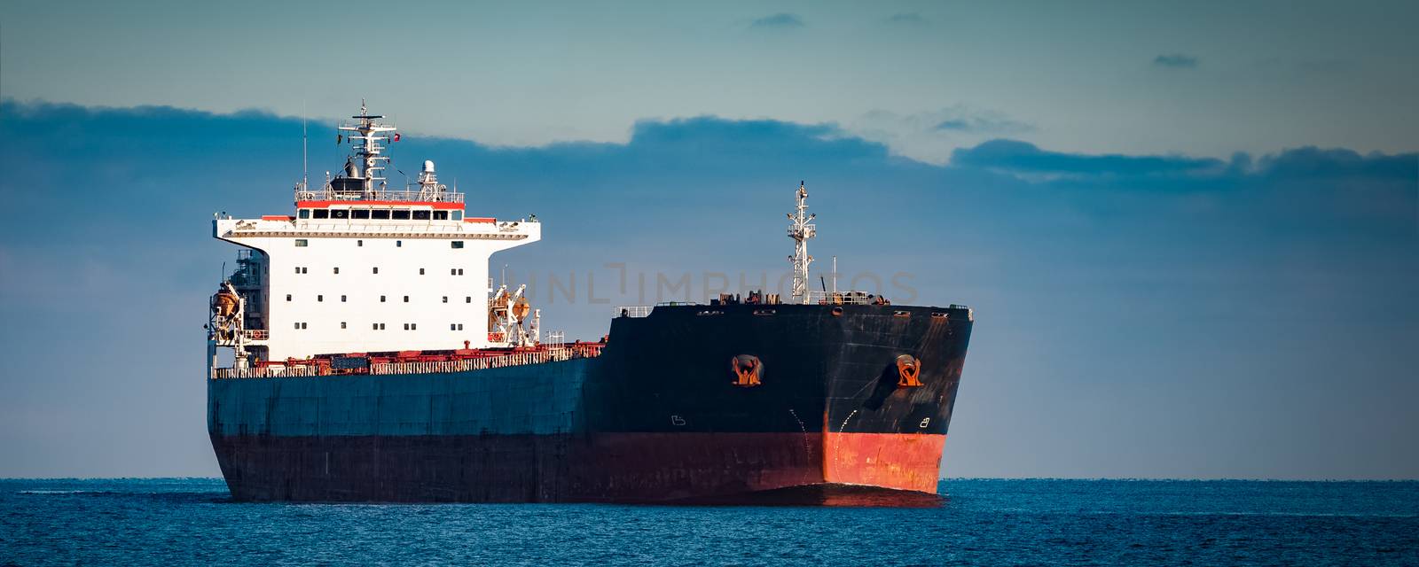 Black cargo ship moving in still Baltic sea water. Riga, Europe