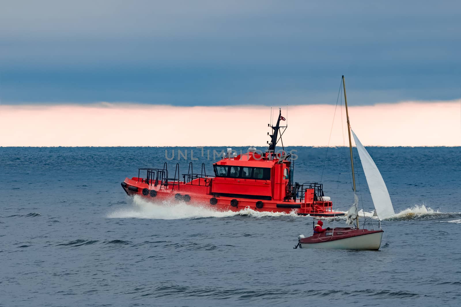 Red pilot ship moving at speed past the sailboat in Baltic sea