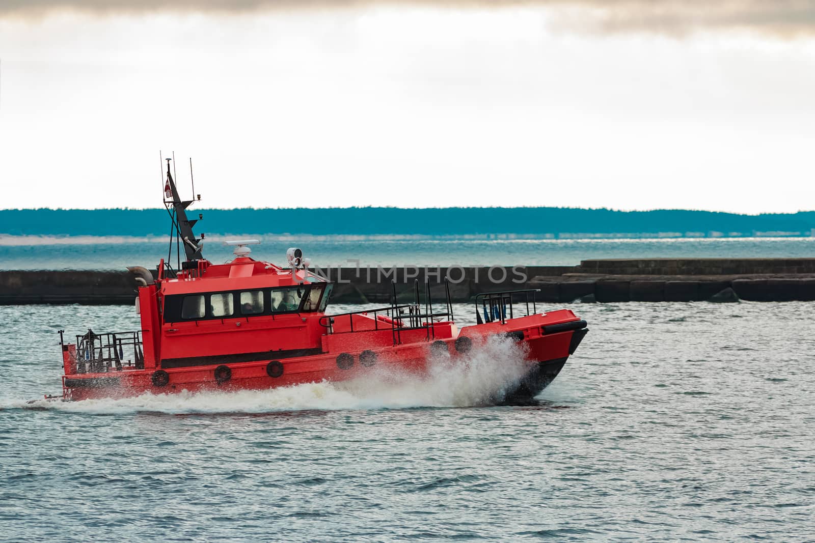 Red pilot ship sailing to Baltic sea past the breakwater dam