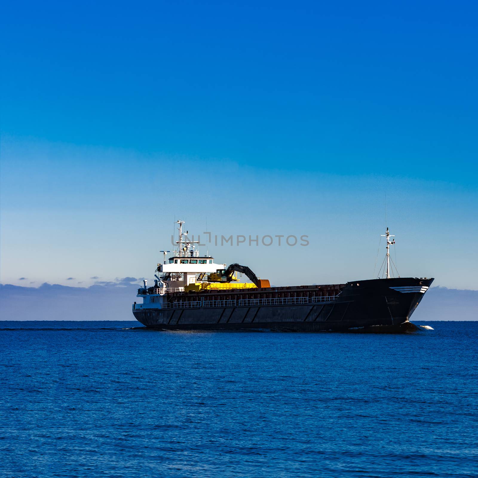 Black cargo ship with long reach excavator moving by baltic sea