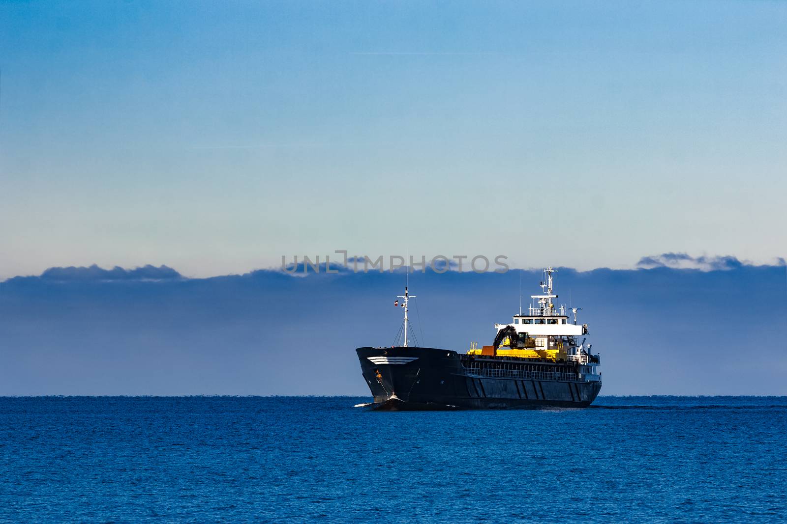 Black cargo ship with long reach excavator moving by baltic sea