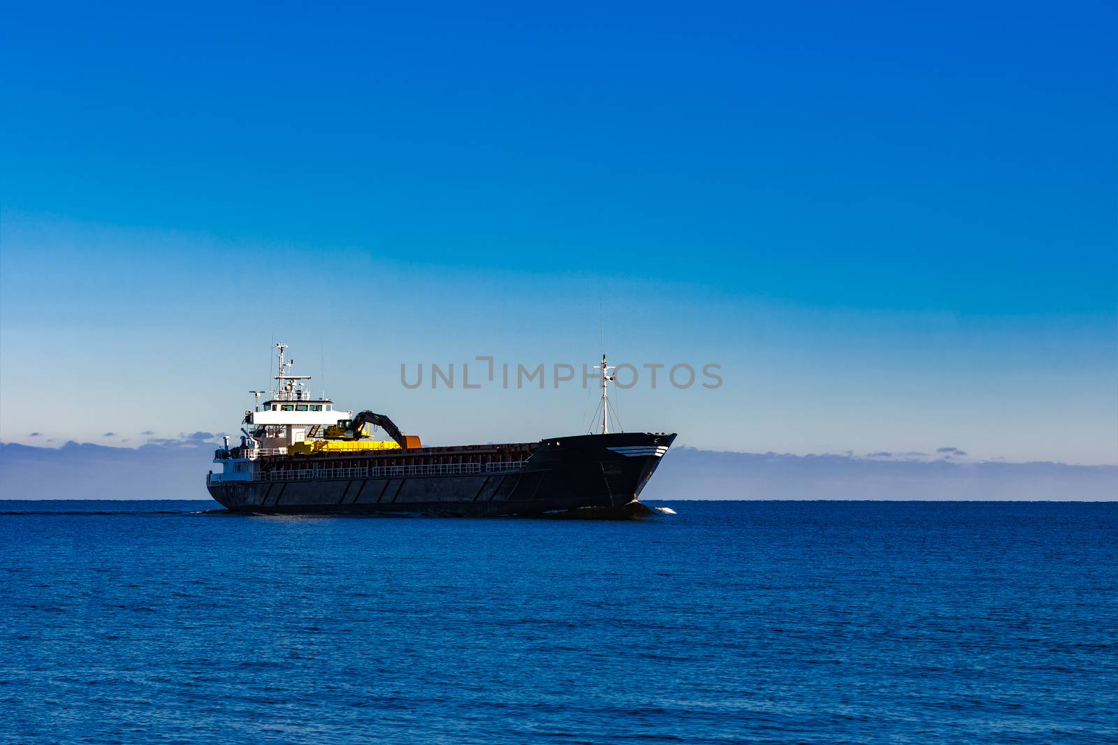 Black cargo ship with long reach excavator moving by baltic sea