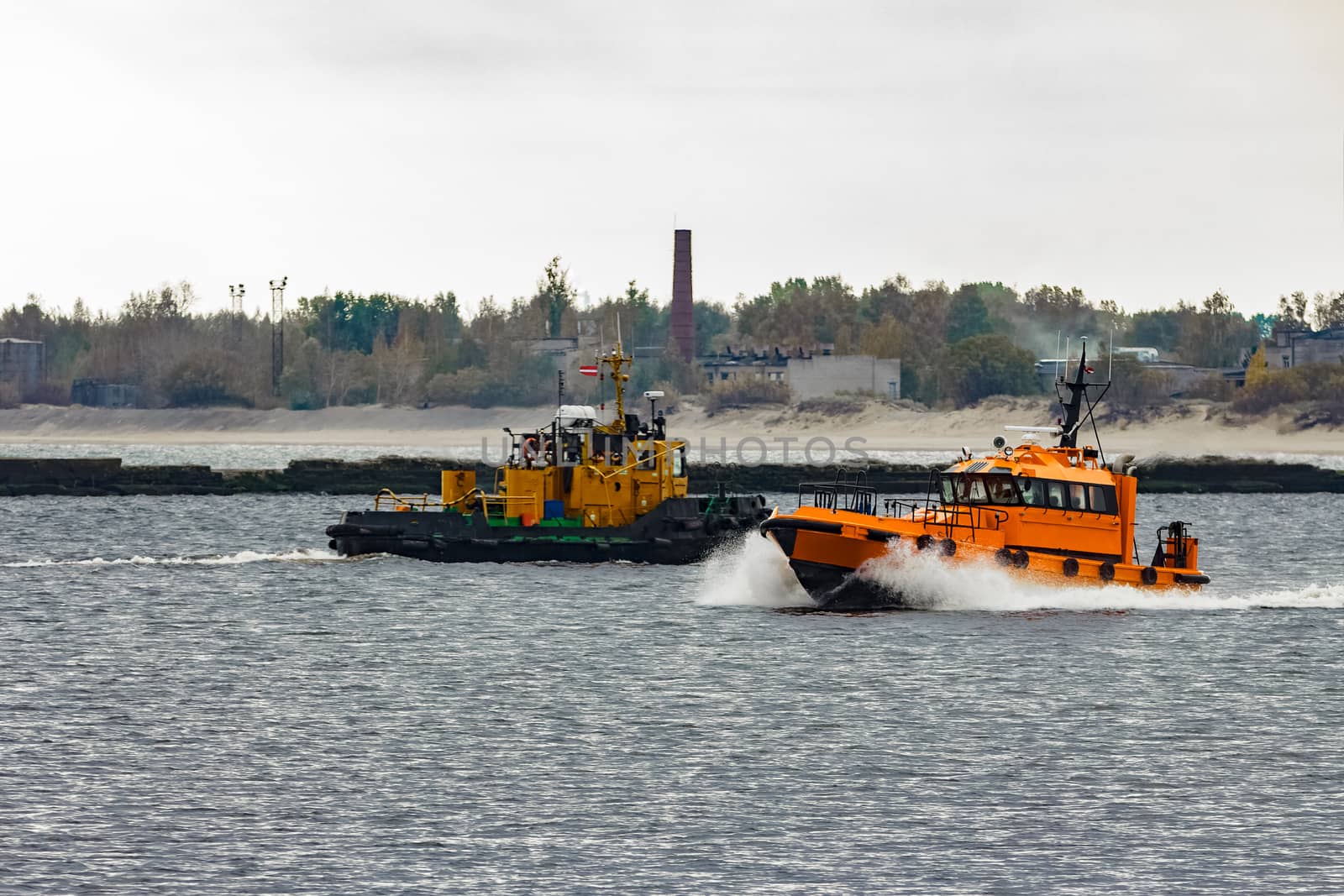 Orange pilot ship moving at speed past the tug ship in Riga