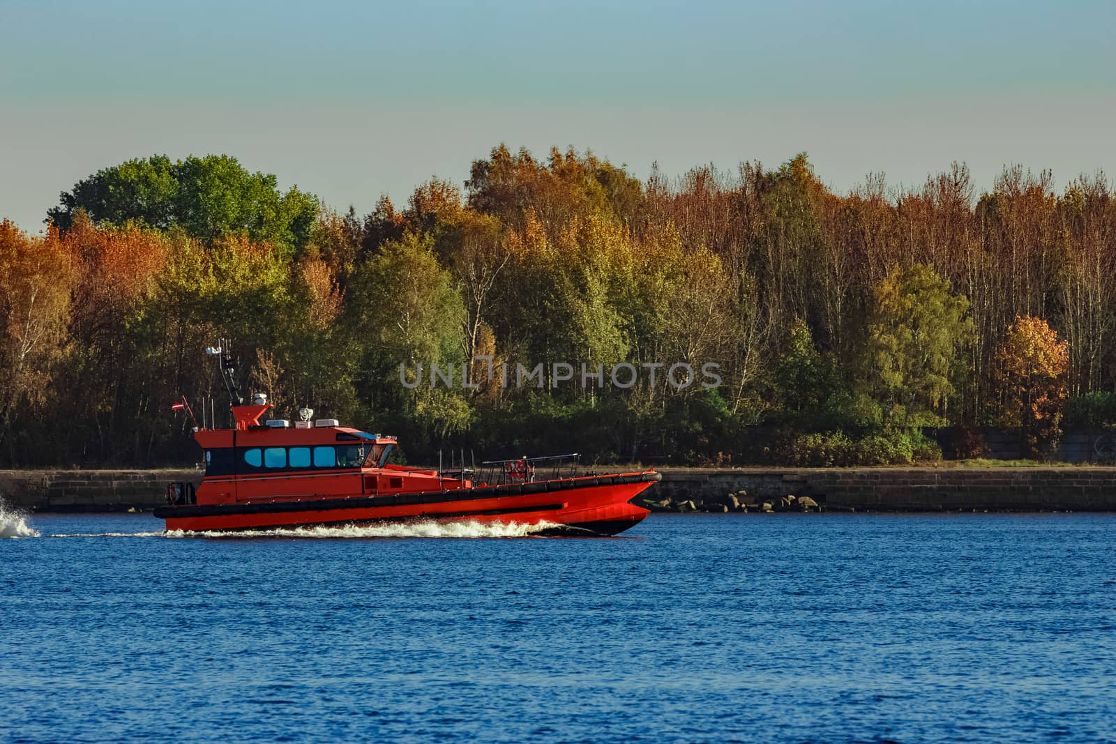 Red pilot ship moving past the autumn trees in Europe