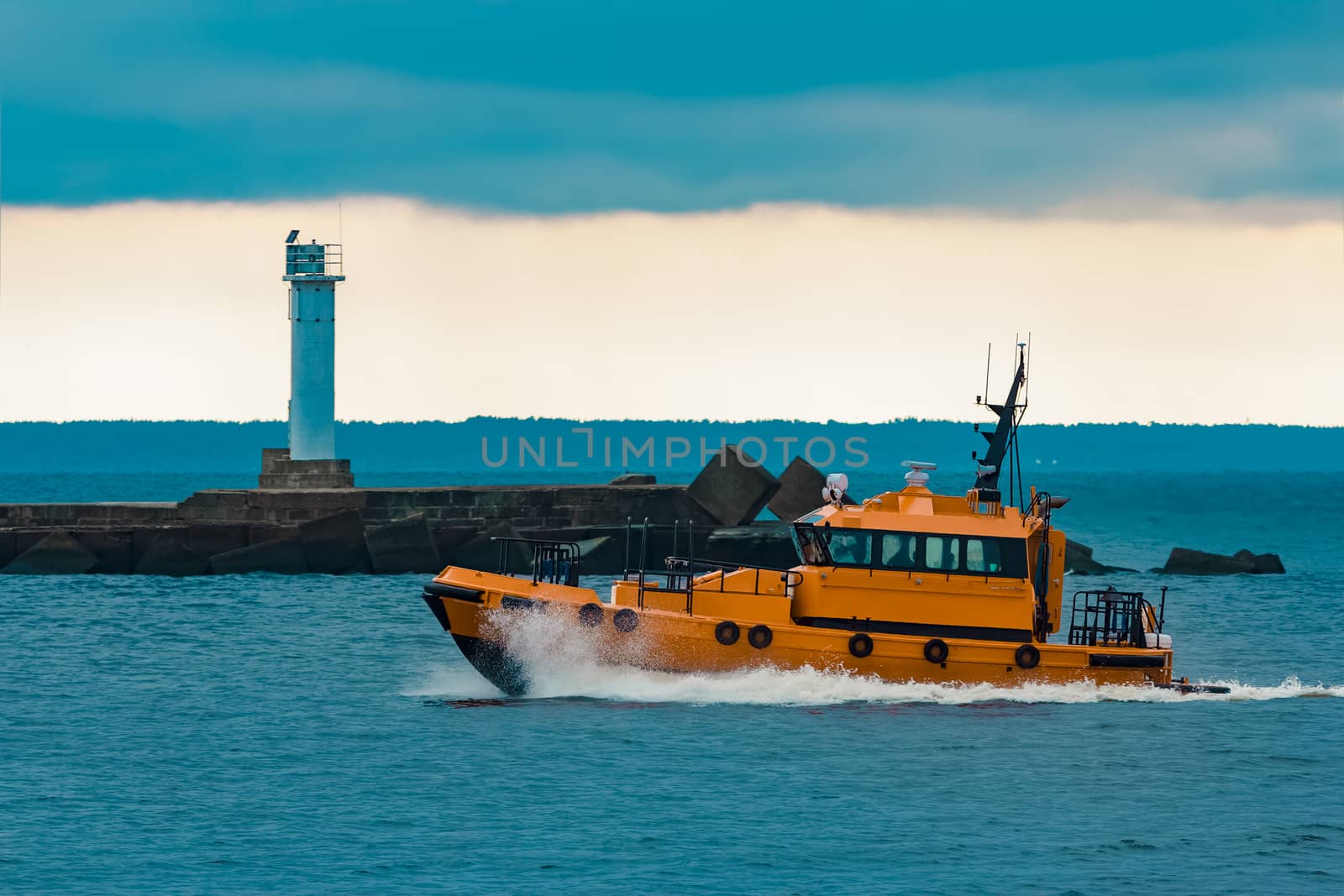 Orange pilot ship moving at speed past the lighthouse in Riga