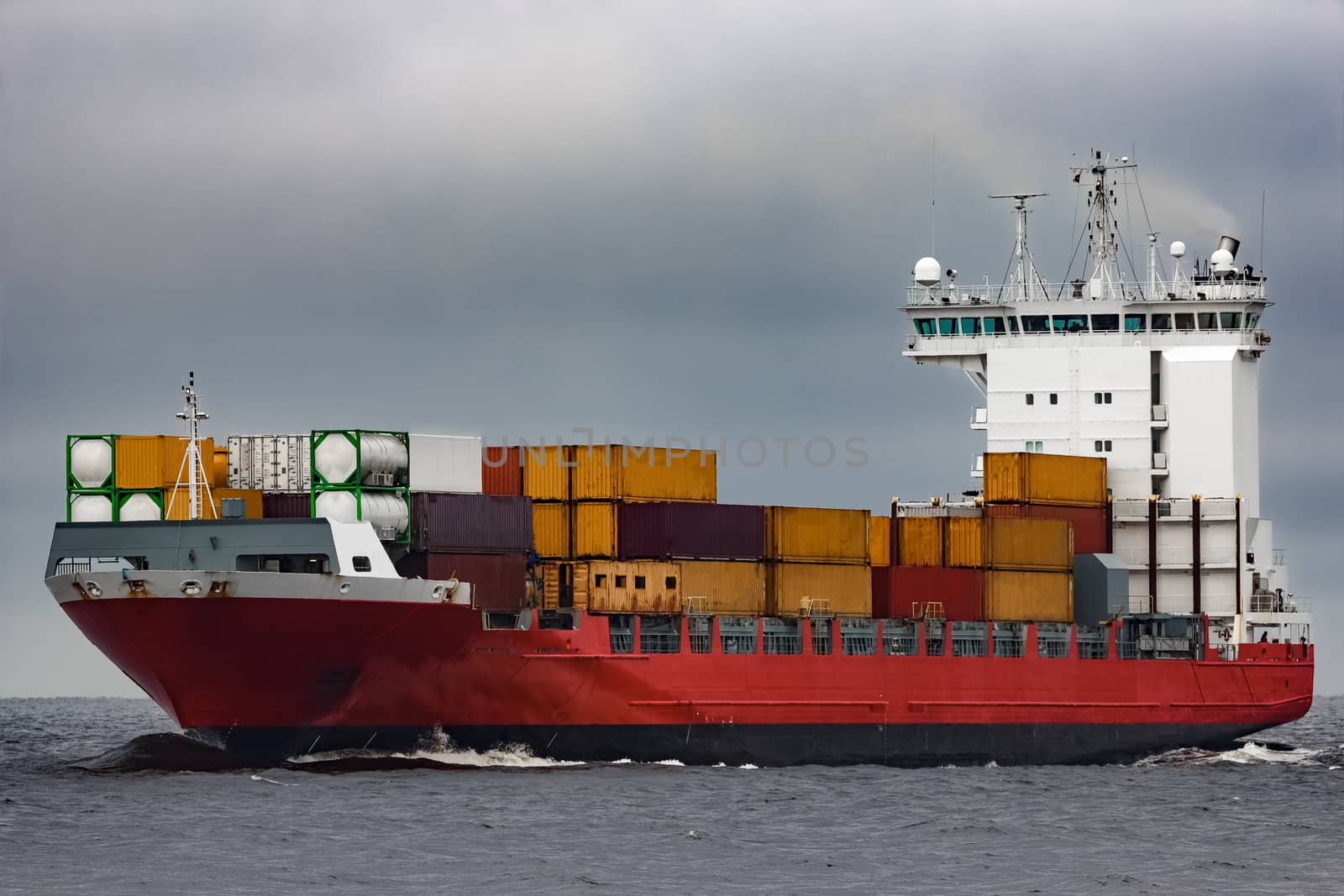Red cargo container ship sailing from Baltic sea in cloudy day