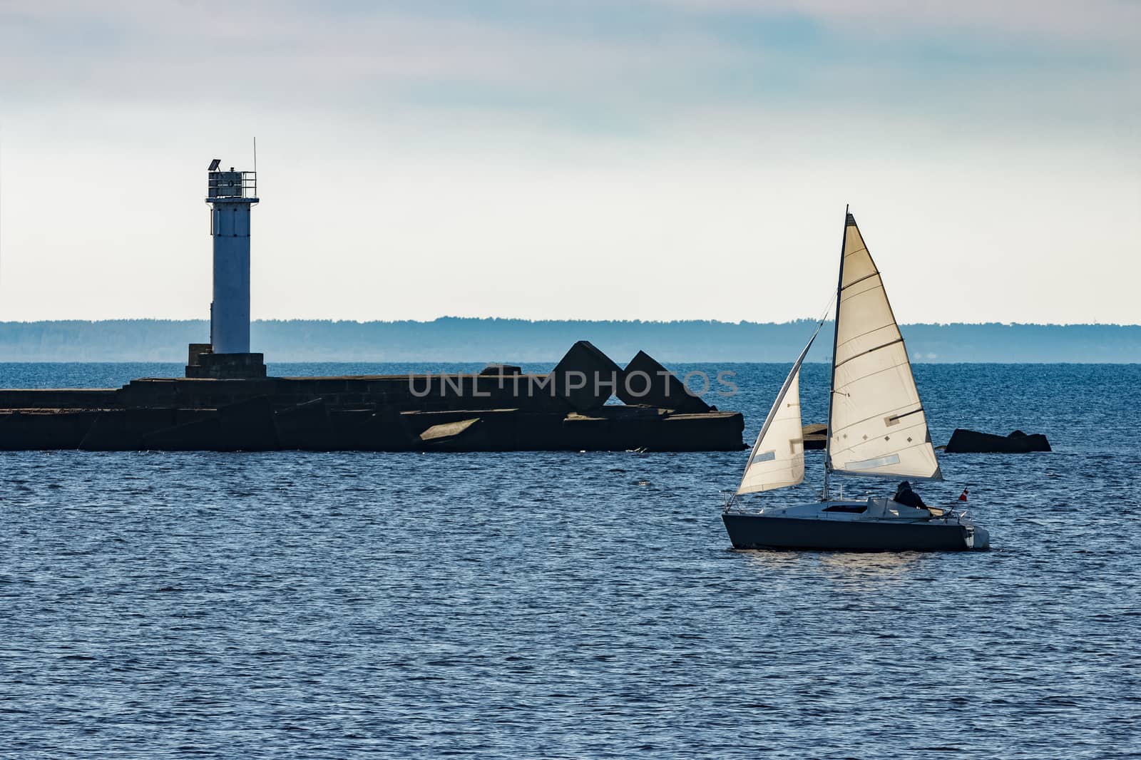 Small sailboat traveling past the lighthouse in sunny day