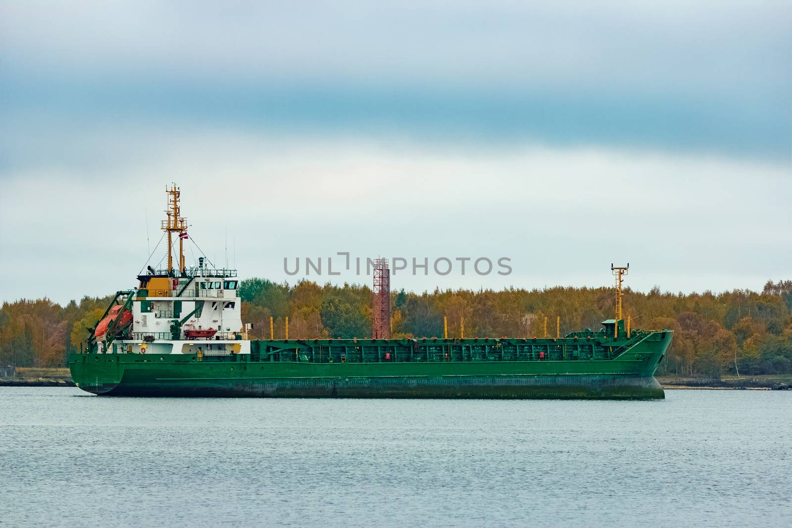 Green cargo ship moving to the port in cloudy day