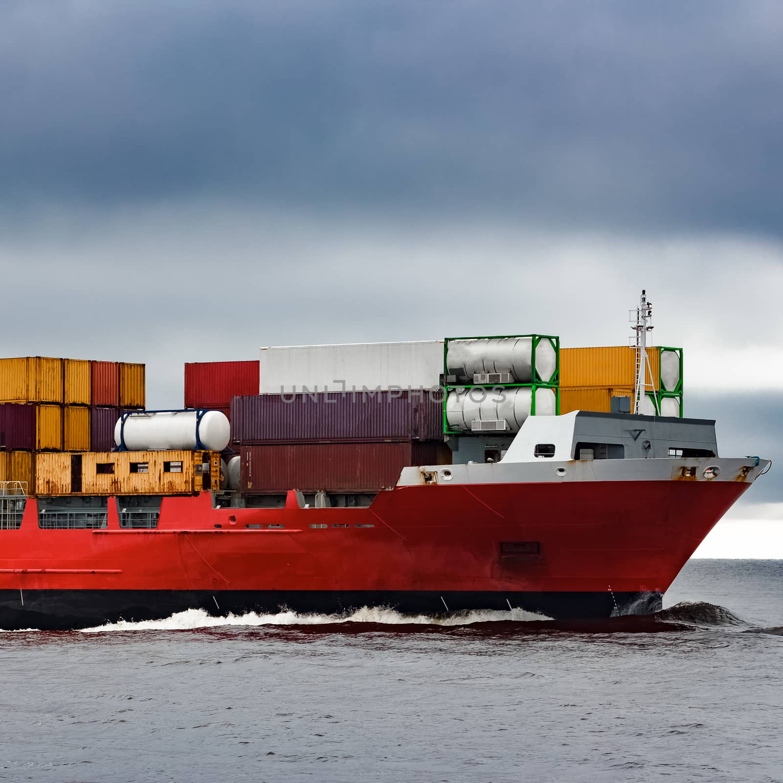 Red cargo container ship's bow in cloudy day