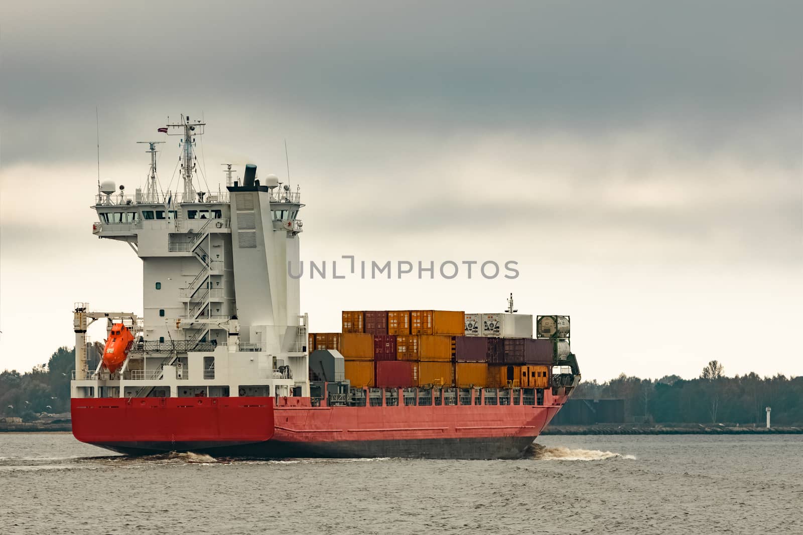 Red cargo container ship entering the port of Riga in cloudy day