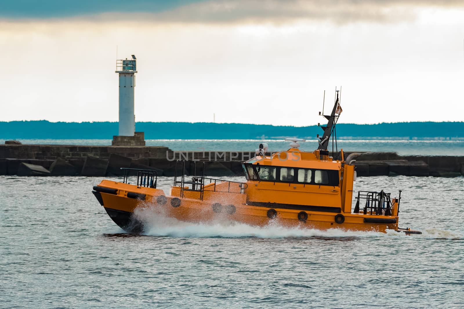 Orange pilot ship moving at speed past the lighthouse in Riga