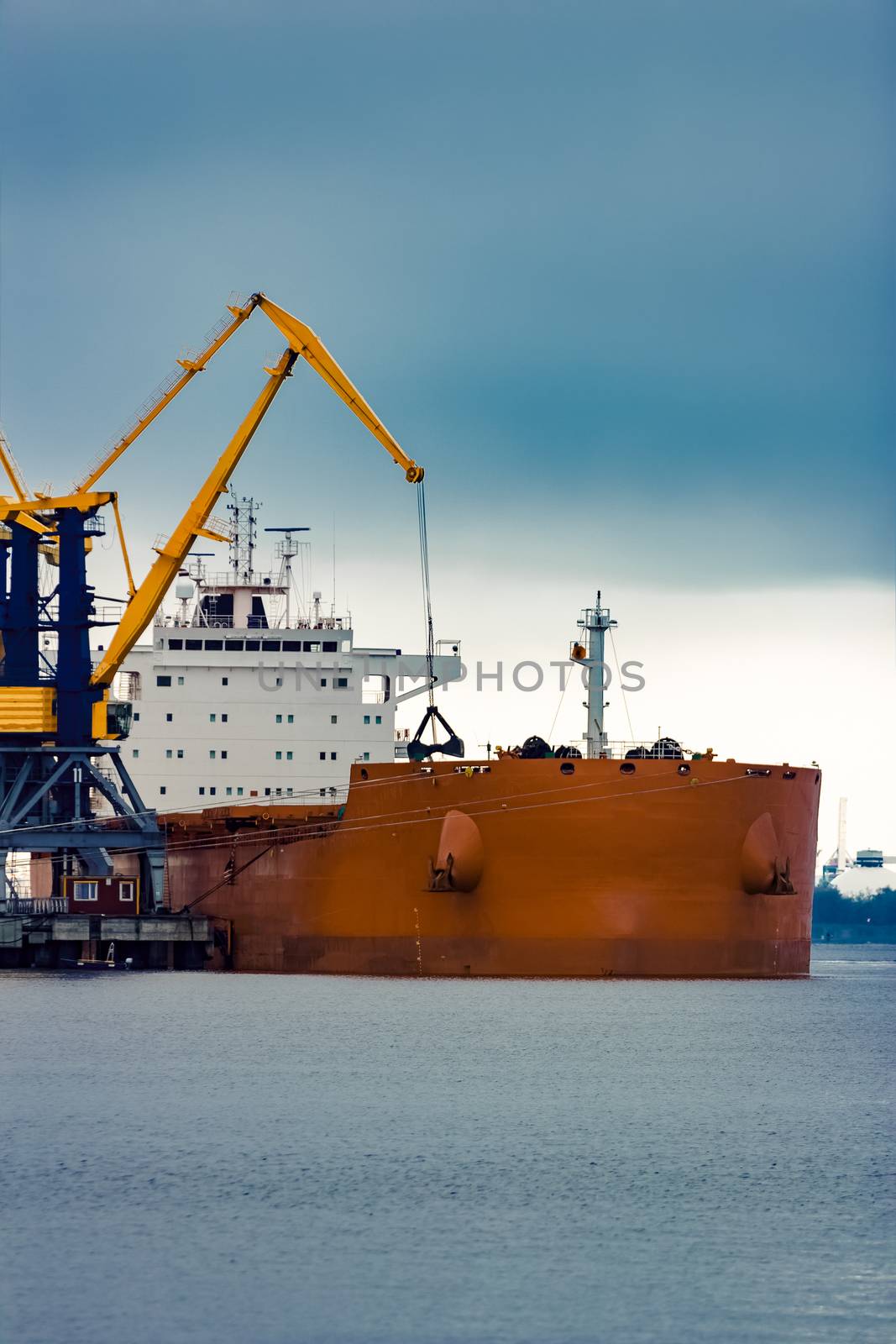 Large orange cargo ship loading with a coal in the port