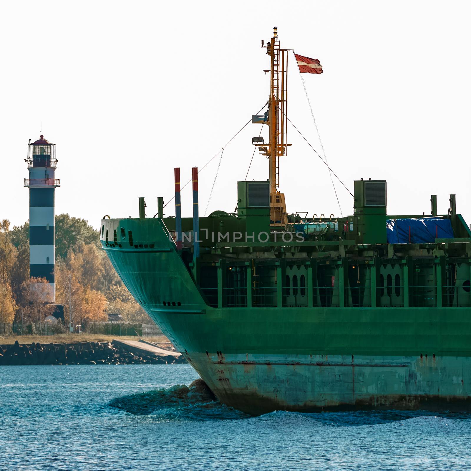 Green cargo ship's bow against lighthouse in still water, Riga