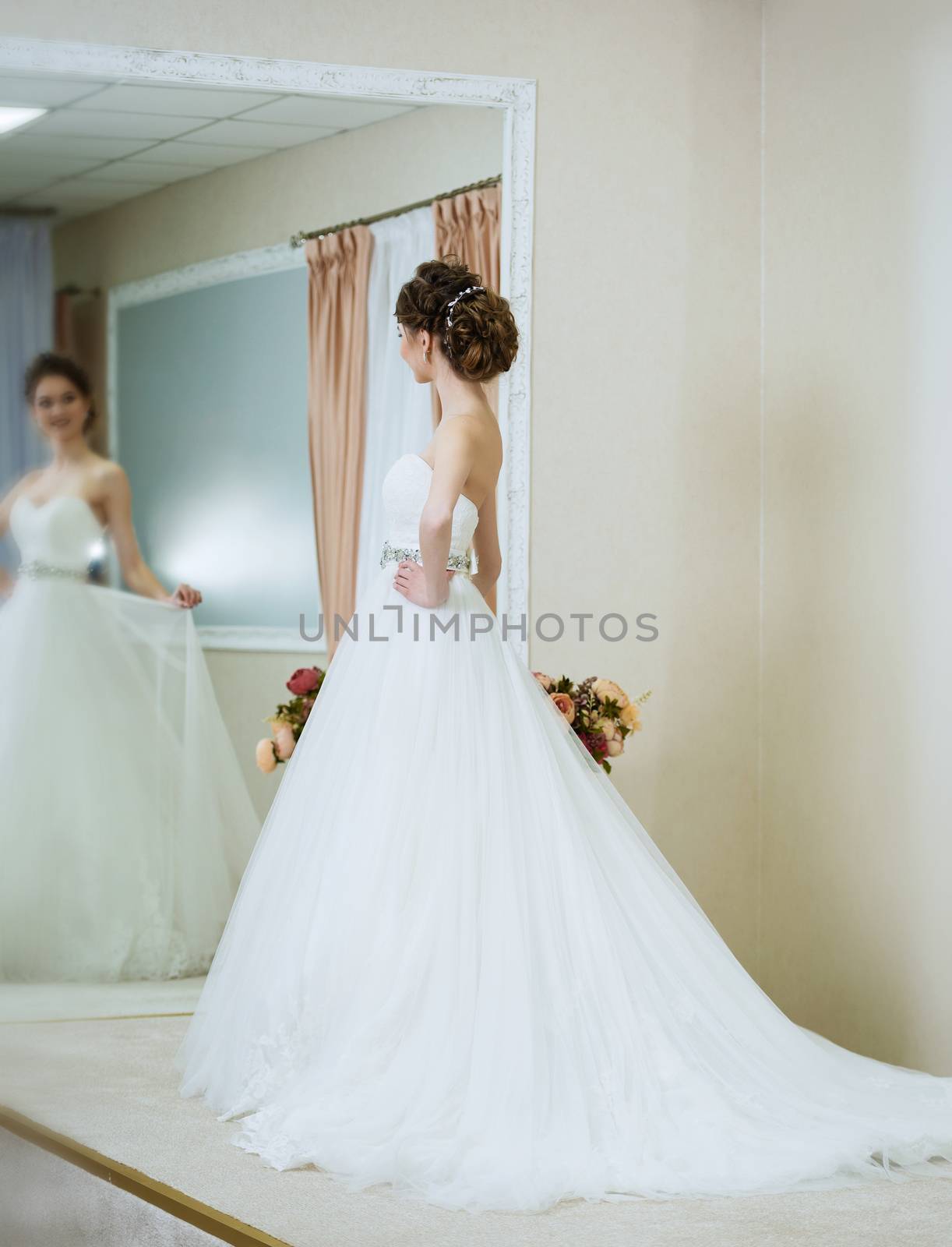 Beautiful young bride in front of the mirror. Portrait with wedding makeup, hairstyle, dress