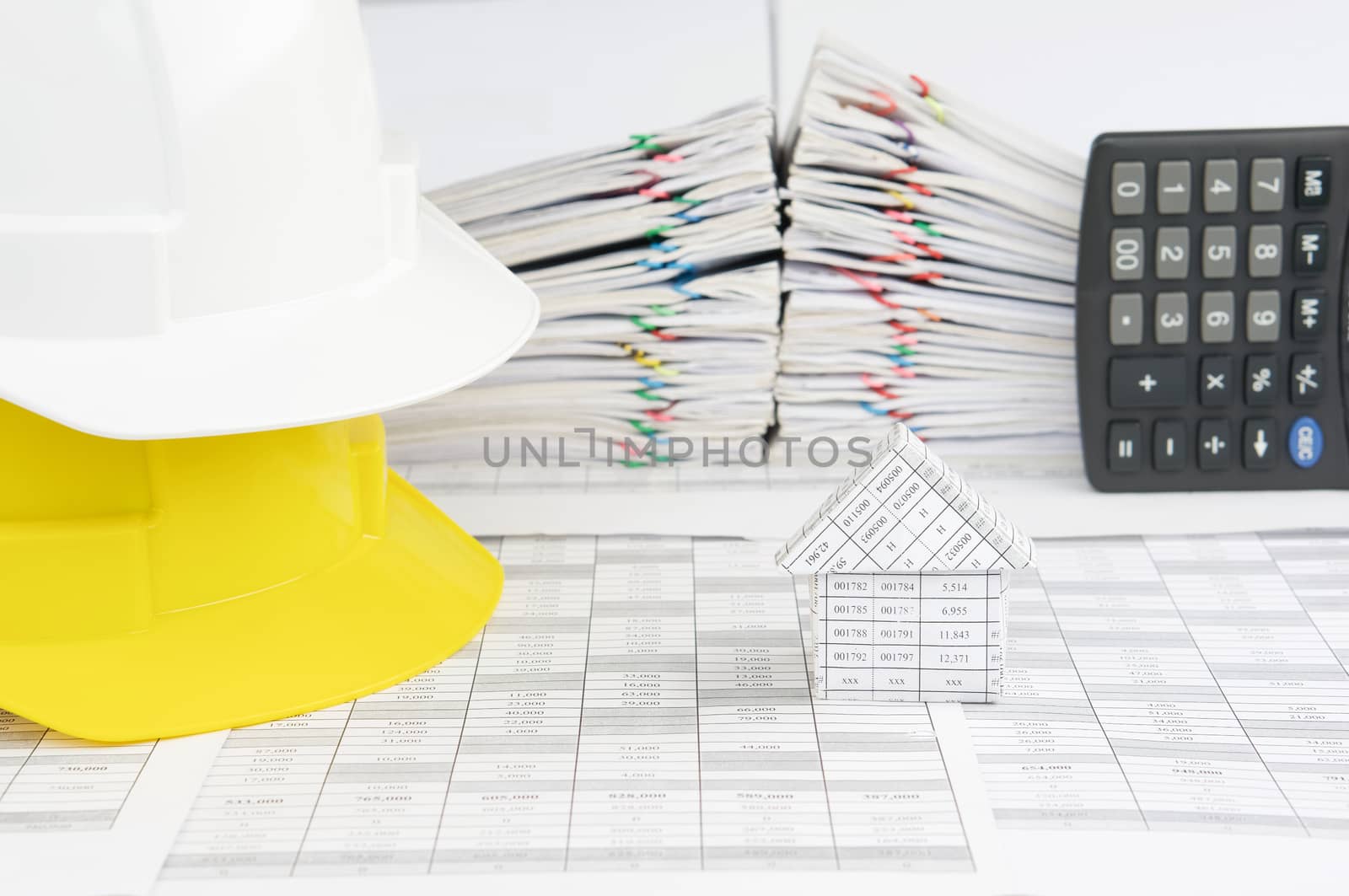 House and white on yellow engineer hat on finance account have blur pile overload document of report and receipt with colorful paperclip with calculator place vertical as background.