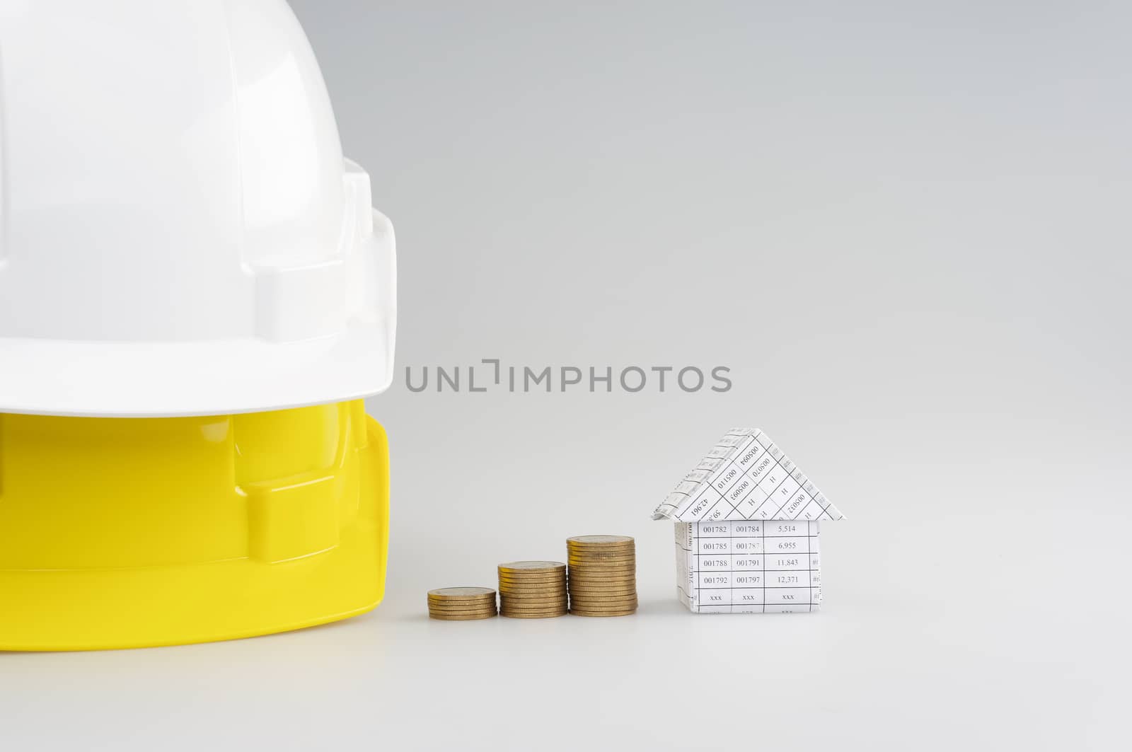 Step pile of gold coins between house and white on yellow engineer hat on white background.