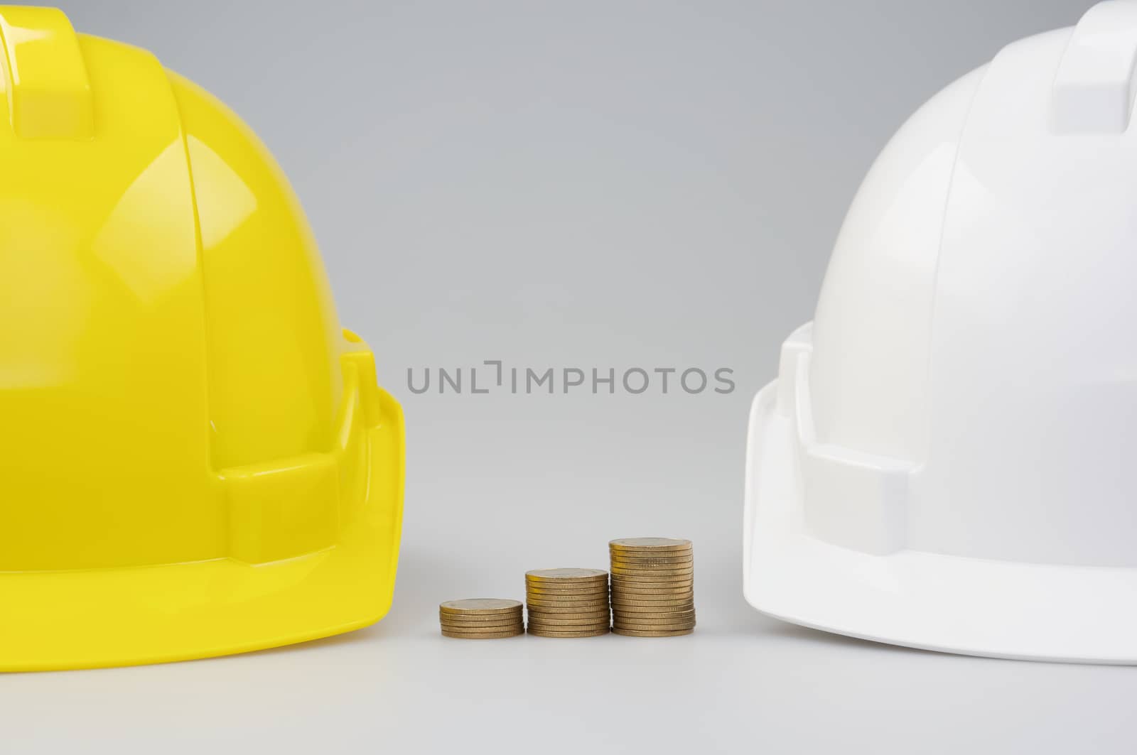 Step pile of gold coins between yellow and white engineer hat on white background.