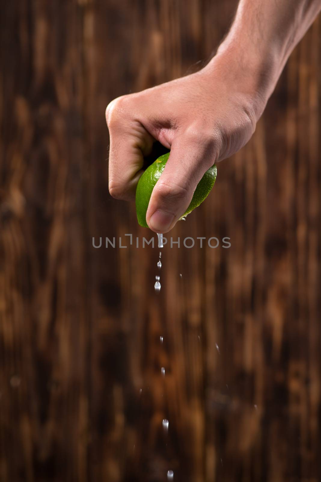 Hand squeeze lime with lime drop on dark wooden background by makidotvn