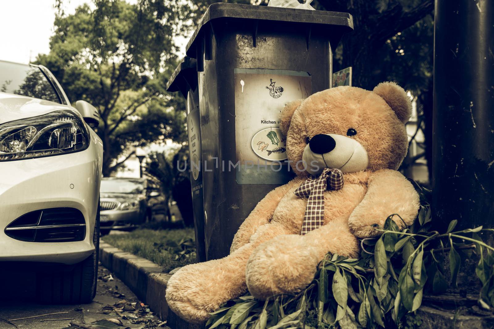 The teddy-bear was throw away sitting beside the garbage trash