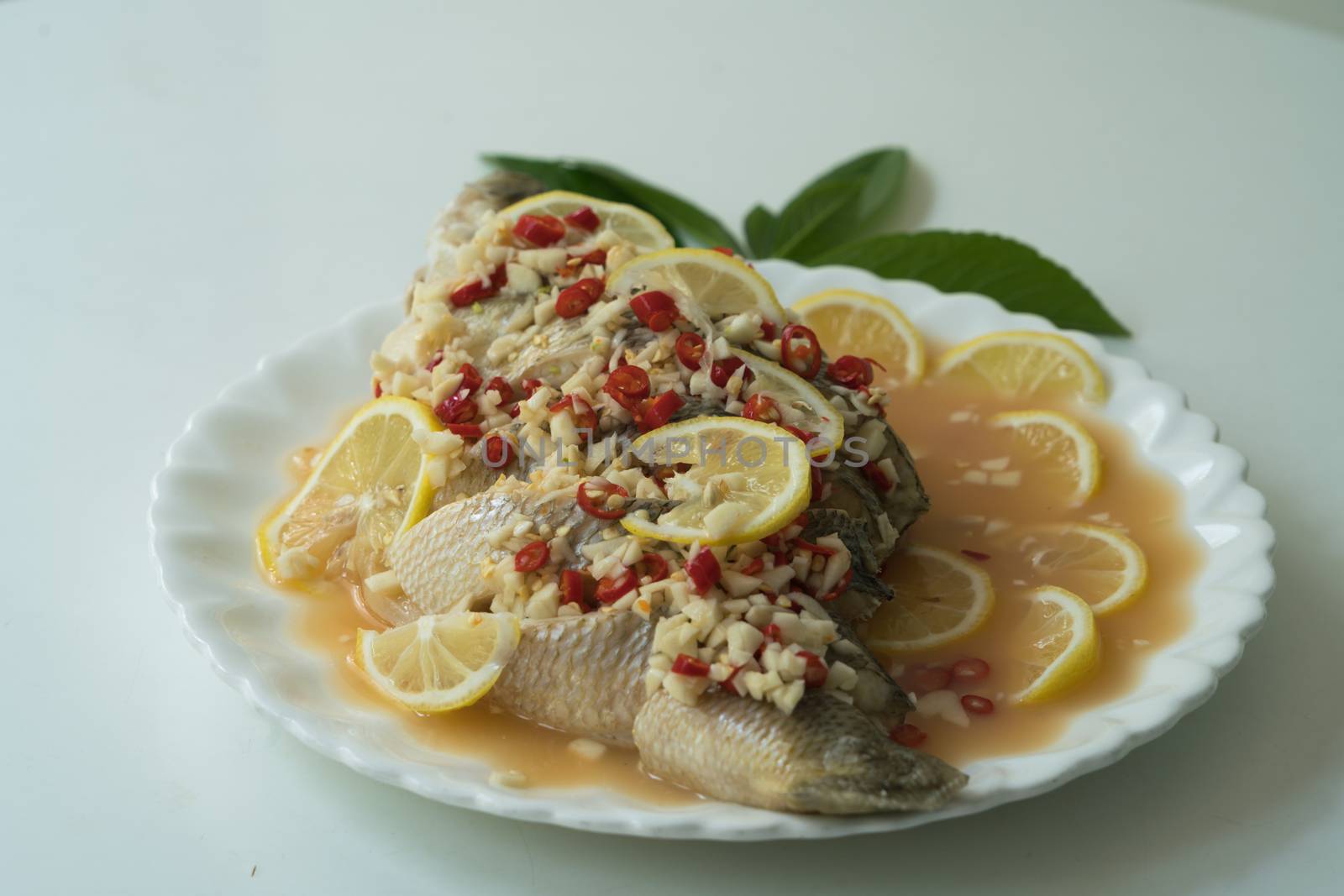 A Seabass steam with lemon, garlic and red chili - Thai food, on white plate