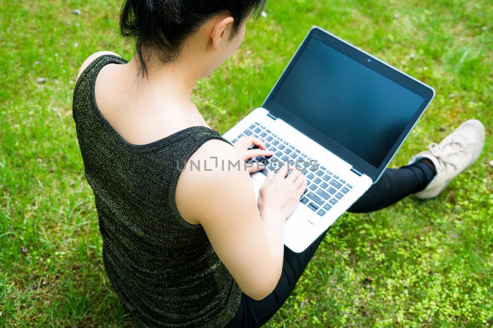 A woman is sitting on the grass while using laptop computer