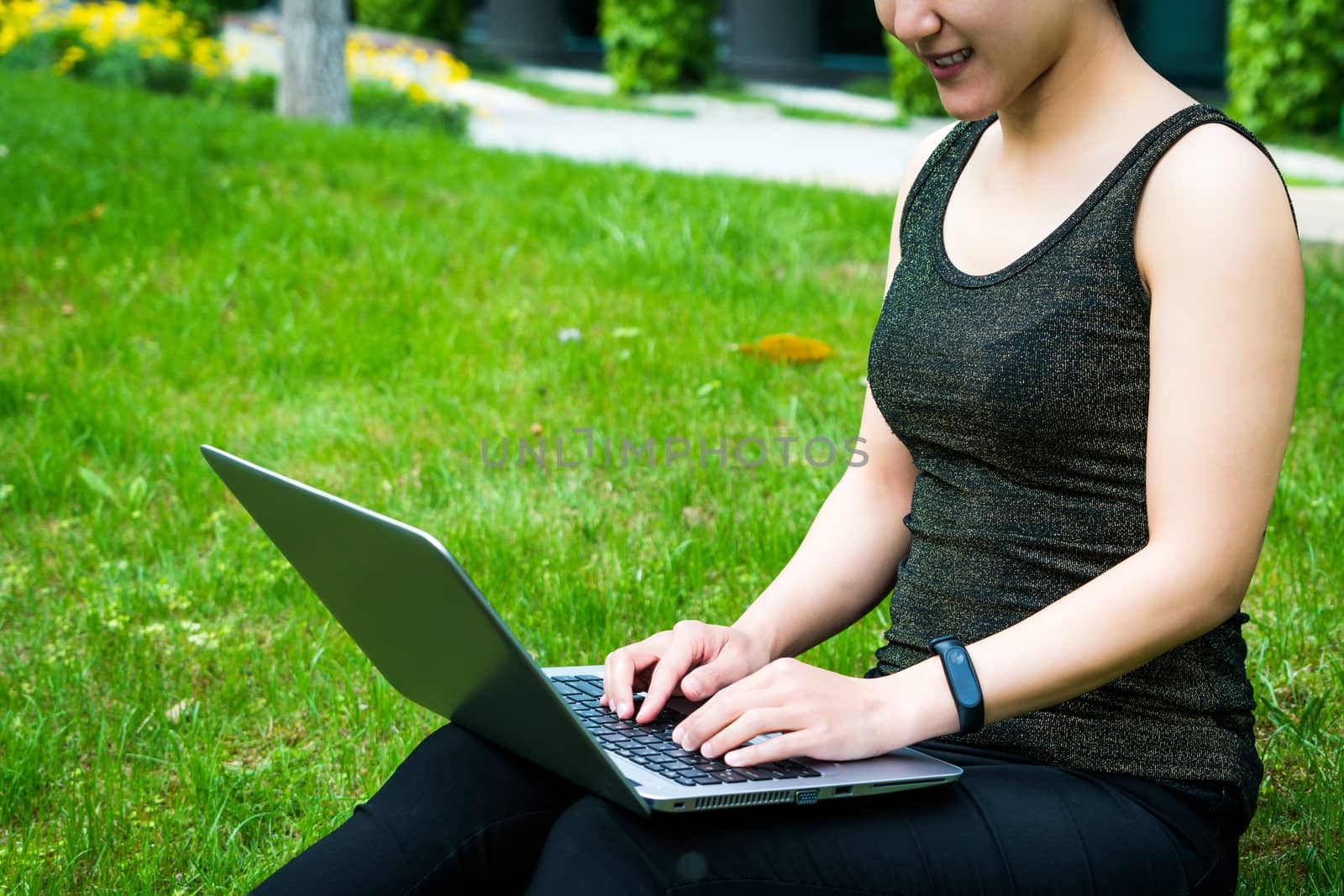 A young woman sitting on the grass is using laptop computer