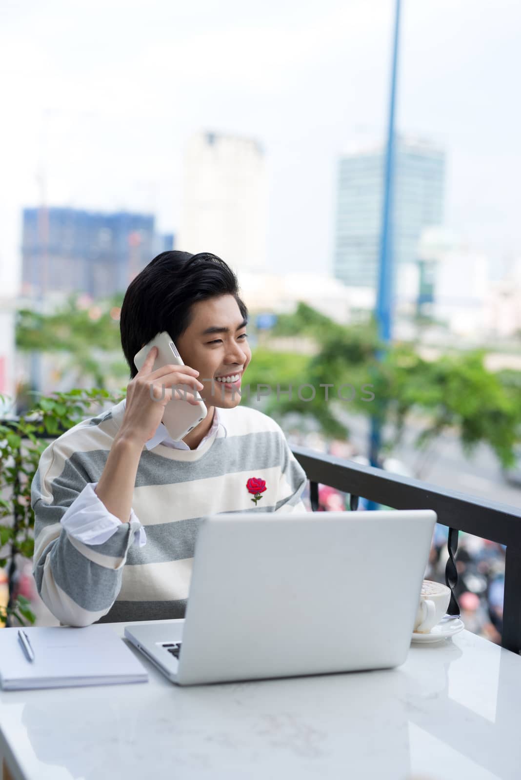 Asian businessman using mobile phone while working with laptop on table in coffee shop