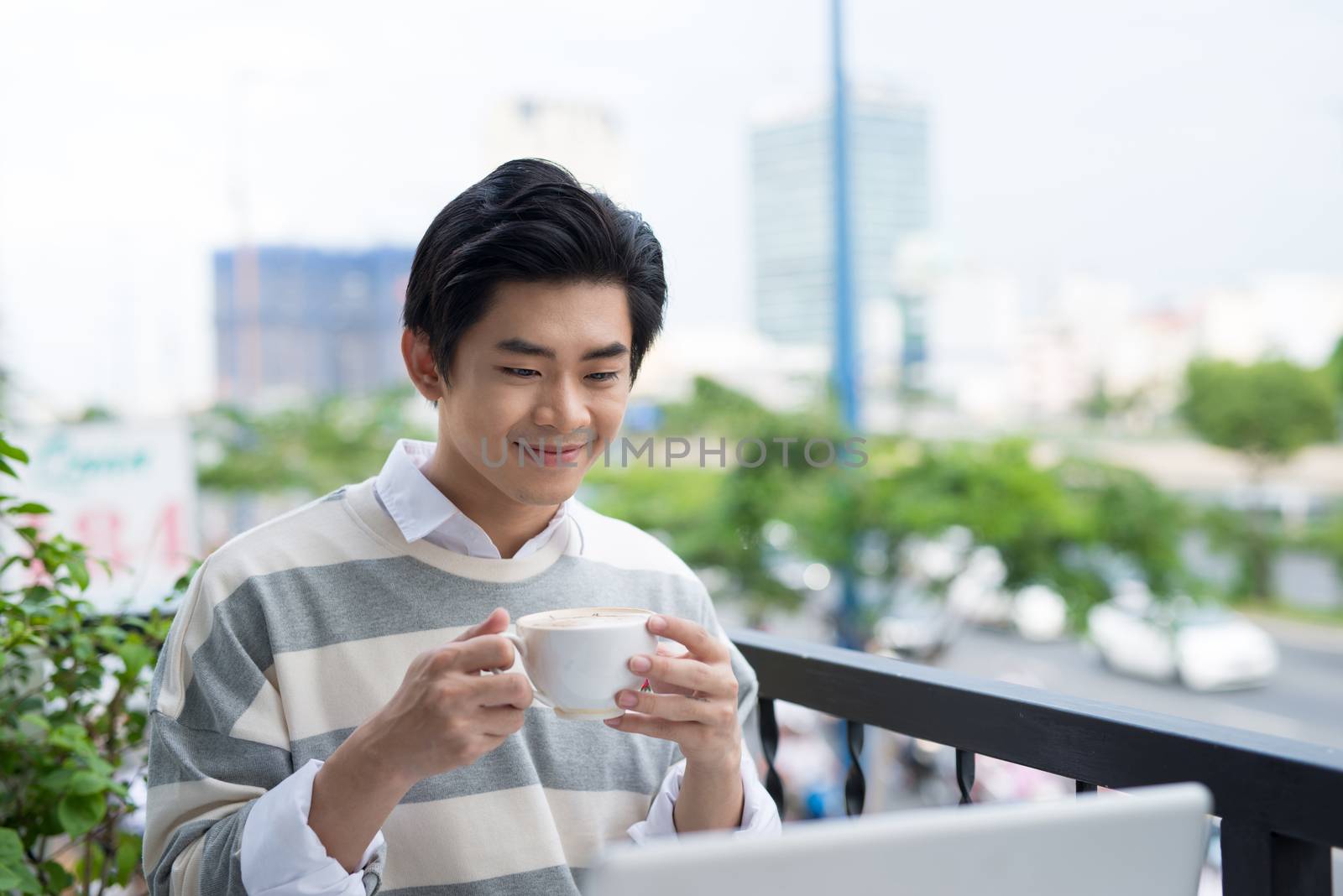 Handsome asian young man working on laptop and smiling while enjoying coffee in cafe