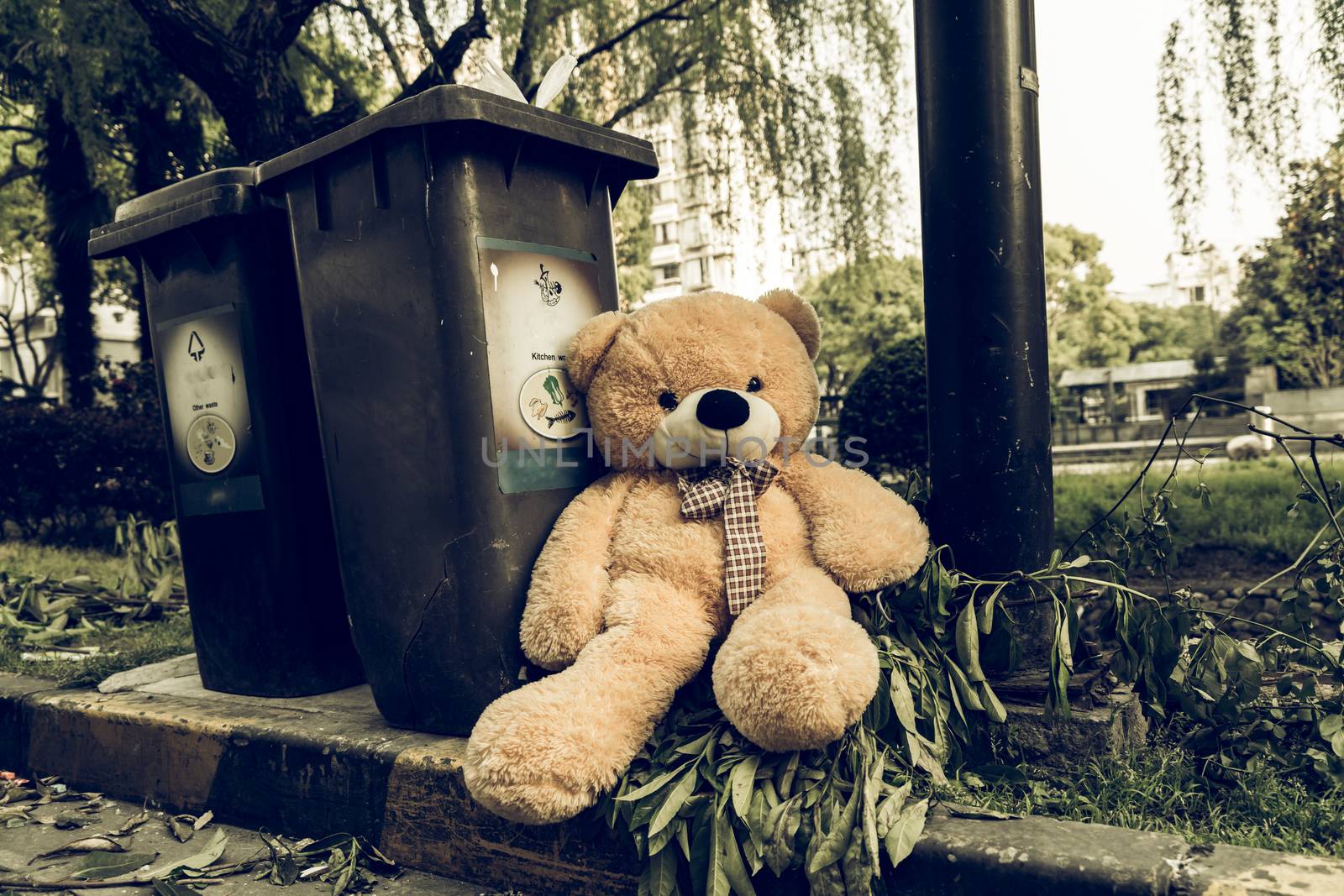 The teddy-bear was throw away sitting beside the garbage trash