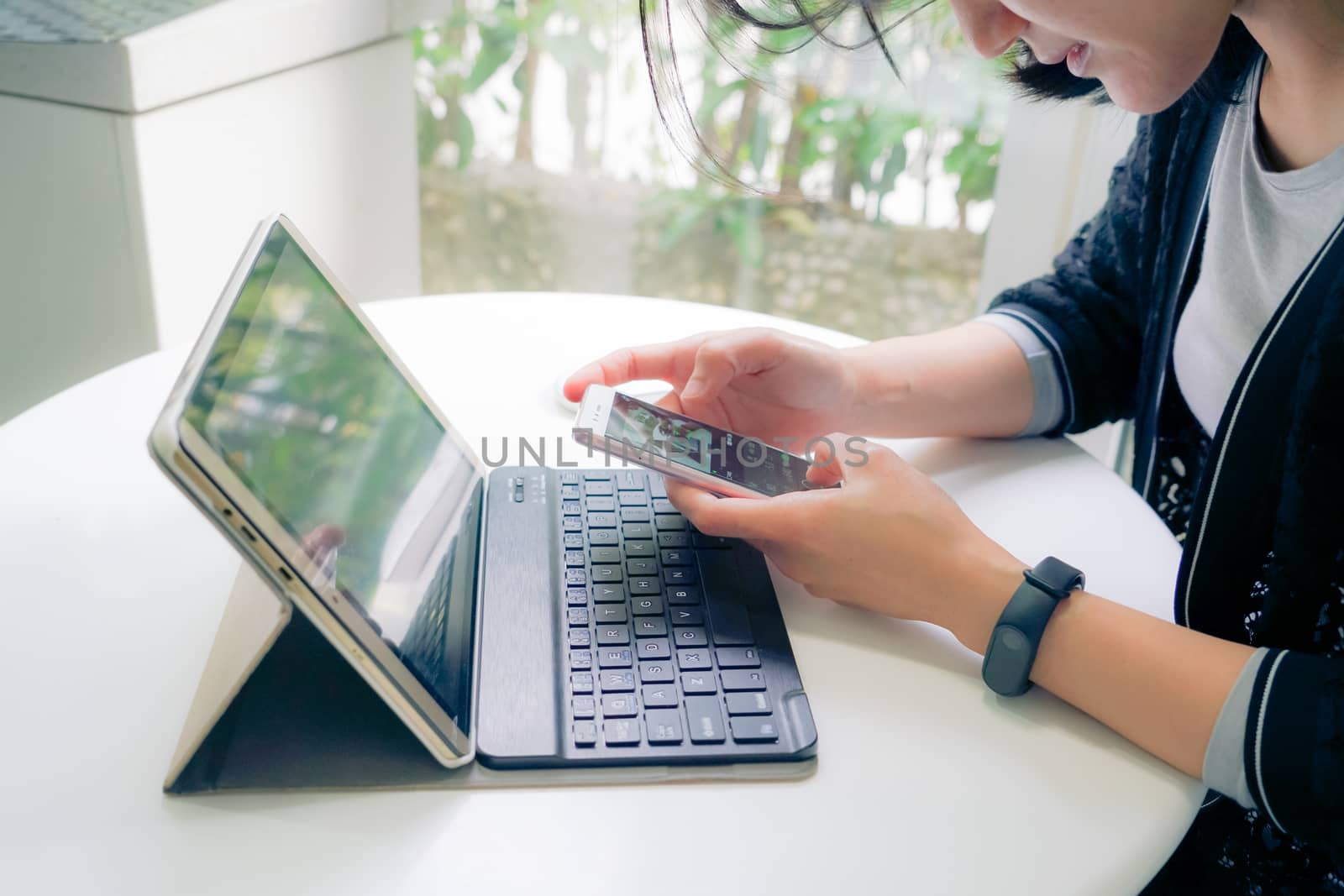 Young student women wearing smart band touching smart phone while using tablet computer