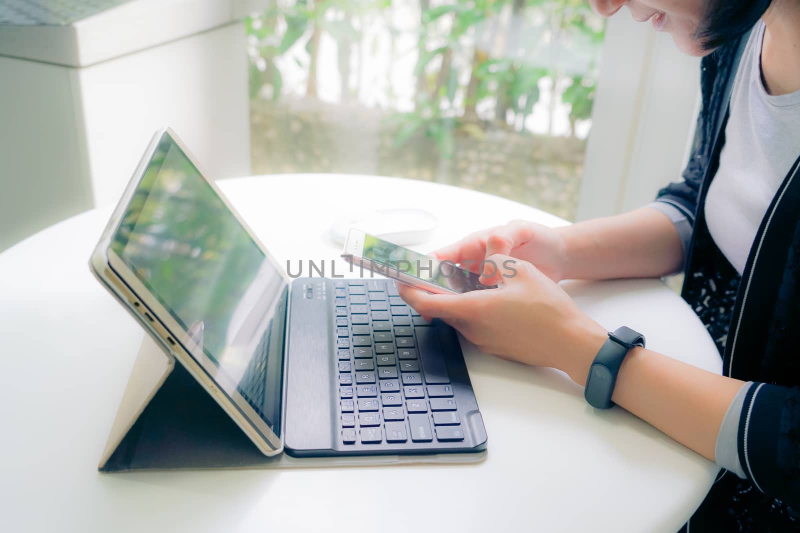 Young student women wearing smart band hold smart phone while using tablet computer