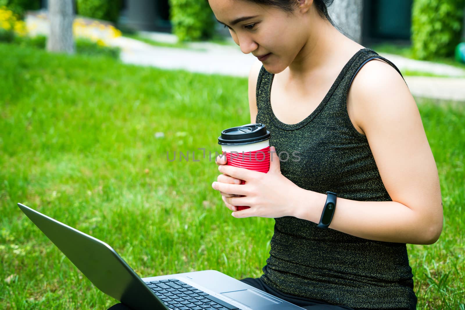 A young woman is looking at laptop computer while holding a red cup of coffee