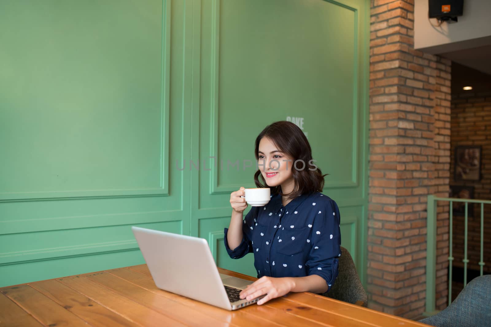 Beautiful cute asian young businesswoman in the cafe, using laptop and drinking coffee smiling