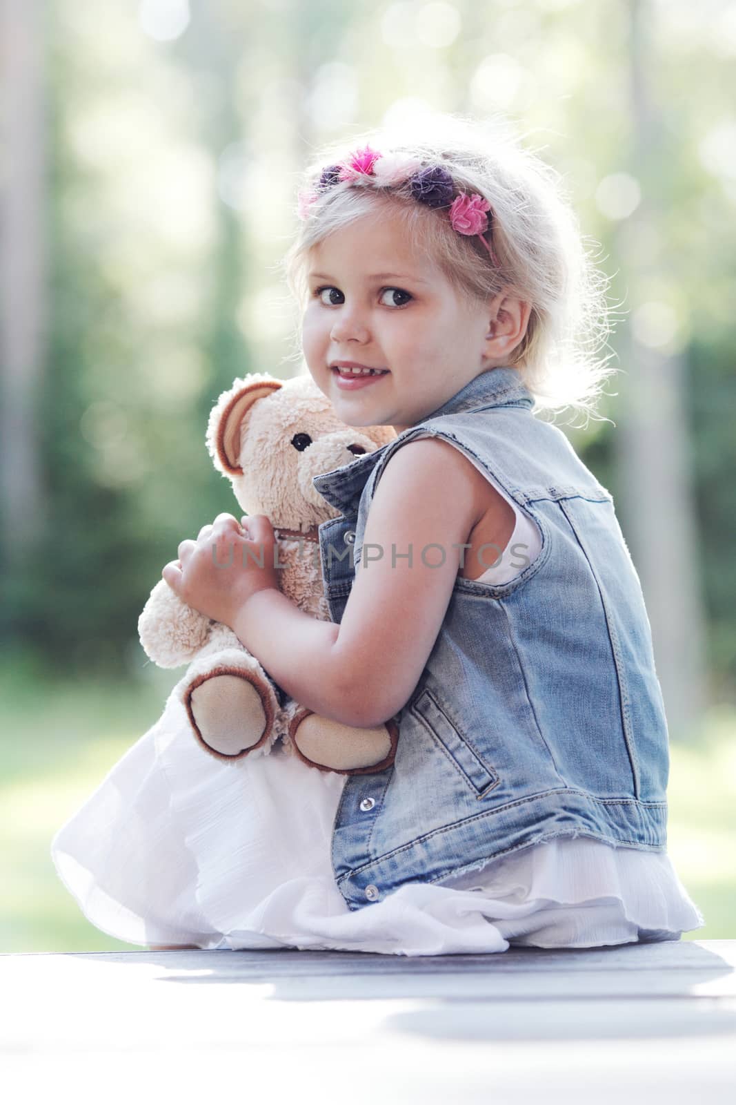 Pretty girl playing with teddy bear outdoors