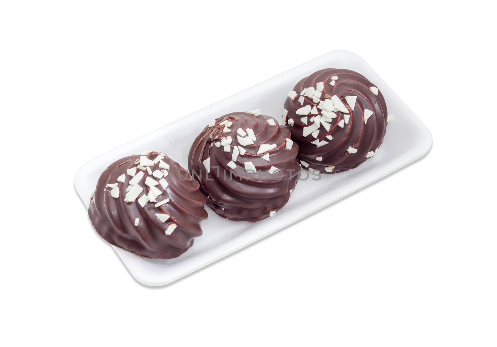 Three cookies with whipped egg whites, glazed with dark chocolate and sprinkled with chunks of white chocolate on the small plastic tray on a light background
