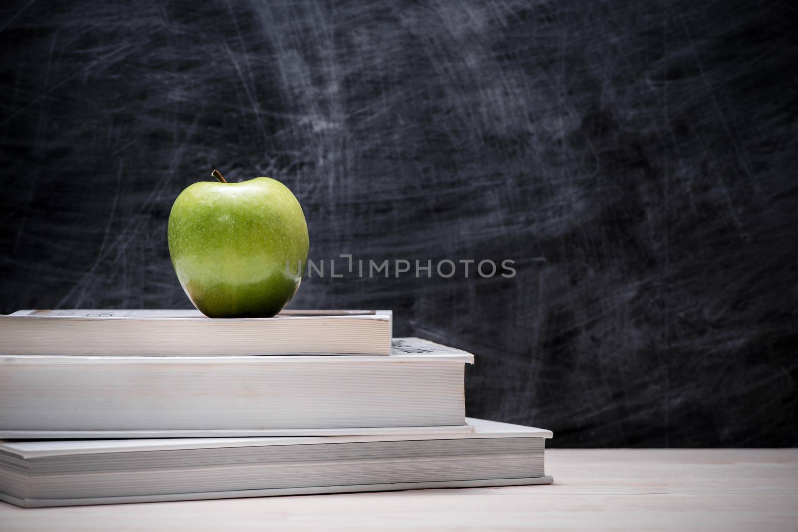 Apple on top of books with chalkboard.