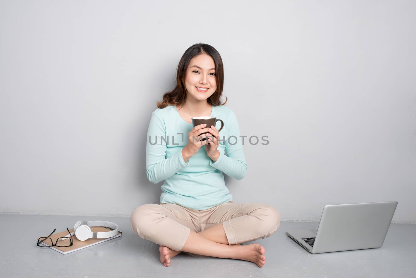 Happy casual beautiful asian woman working on a laptop sitting on floor at home.